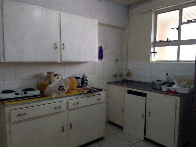 A dated kitchen featuring original cabinetry, tiled backsplash, and a stainless steel sink, requiring modernization and repair of damaged fixtures.