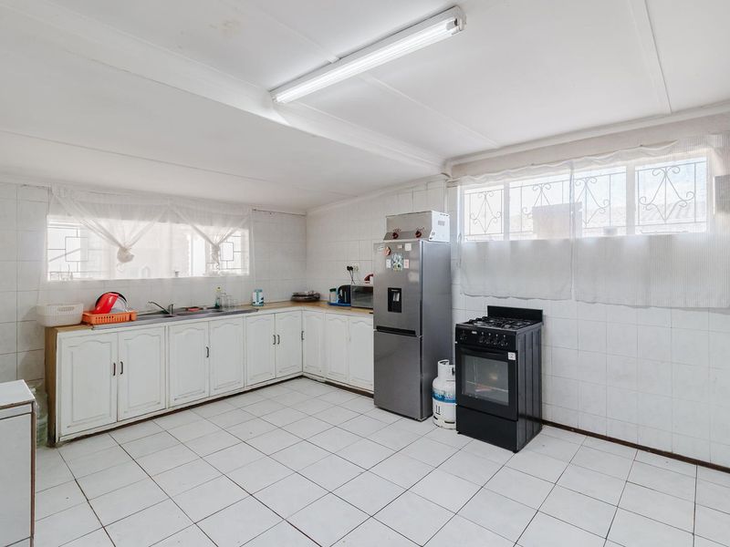 A functional kitchen featuring white cabinetry, tiled walls and flooring, and security bars on the windows, offering potential for a modern renovation.