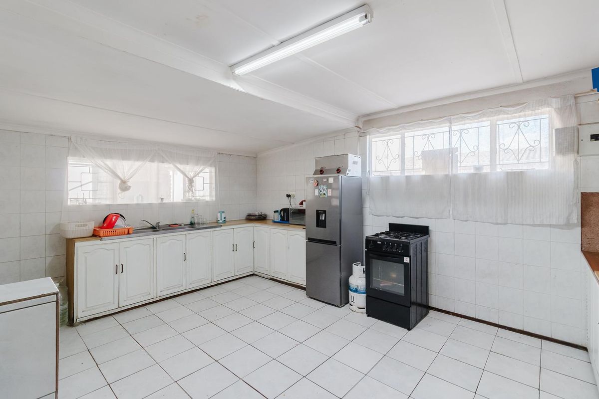 A functional kitchen featuring white cabinetry, tiled walls and flooring, and security bars on the windows, offering potential for a modern renovation.