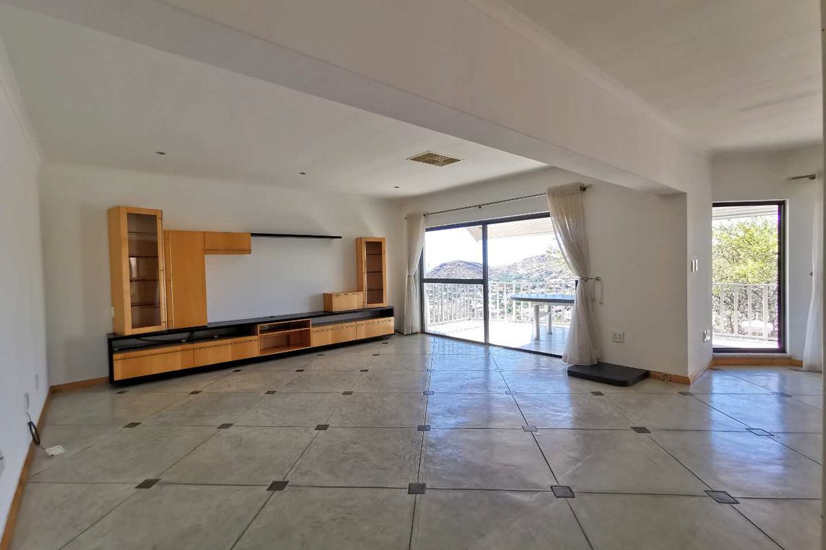 Spacious living area featuring large format floor tiles, built-in cabinetry, and sliding glass doors opening onto a balcony with scenic views.