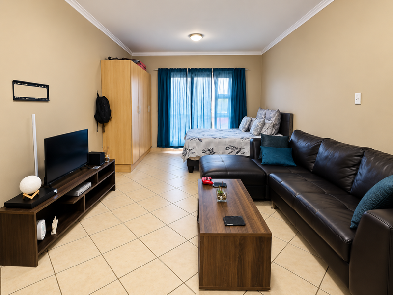 An open-plan living and bedroom area featuring tiled flooring, a built-in wardrobe, and access to a balcony through sliding glass doors.