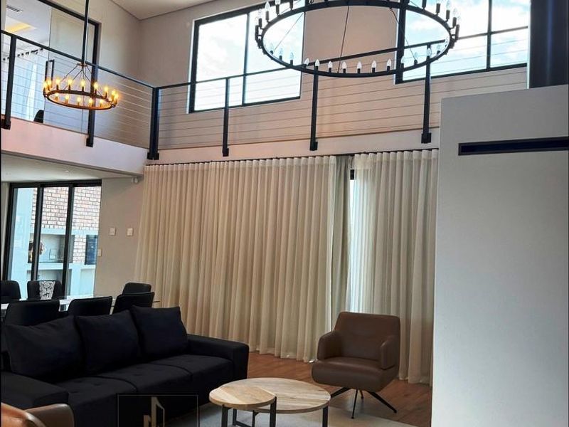Spacious open-plan living area featuring double volume ceilings, a mezzanine level, large windows, and modern lighting fixtures with high-quality hardwood flooring.