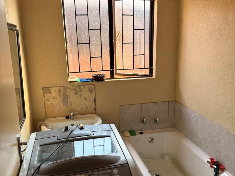 A functional laundry and bathroom space featuring a built-in bathtub, wall-mounted basin, and security bars on the window.