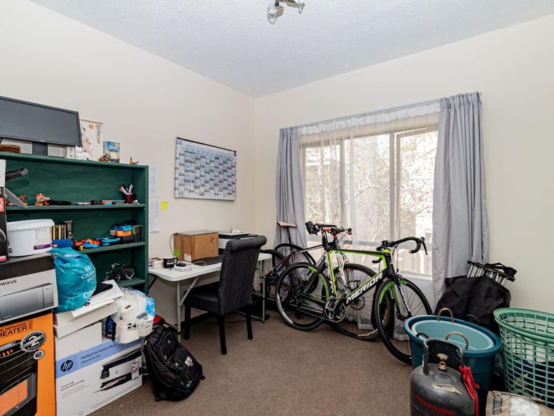 A bedroom featuring carpet flooring and a large sliding window, currently utilized as a home office and storage space.