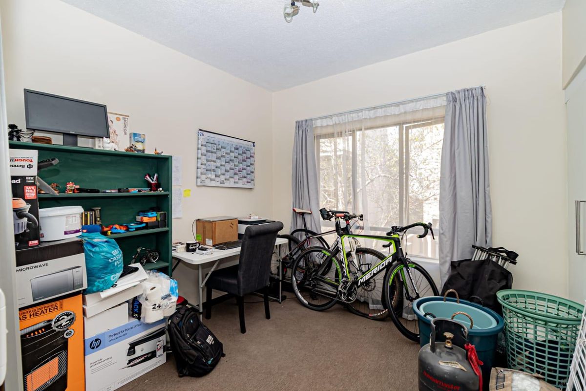 A bedroom featuring carpet flooring and a large sliding window, currently utilized as a home office and storage space.