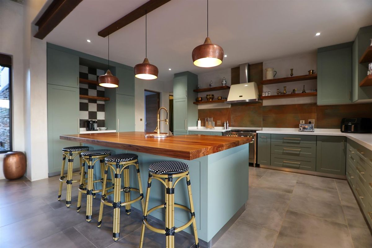 Modern kitchen featuring sage green cabinetry, a large wooden island with a breakfast bar, copper pendant lighting, and a professional-style range cooker.
