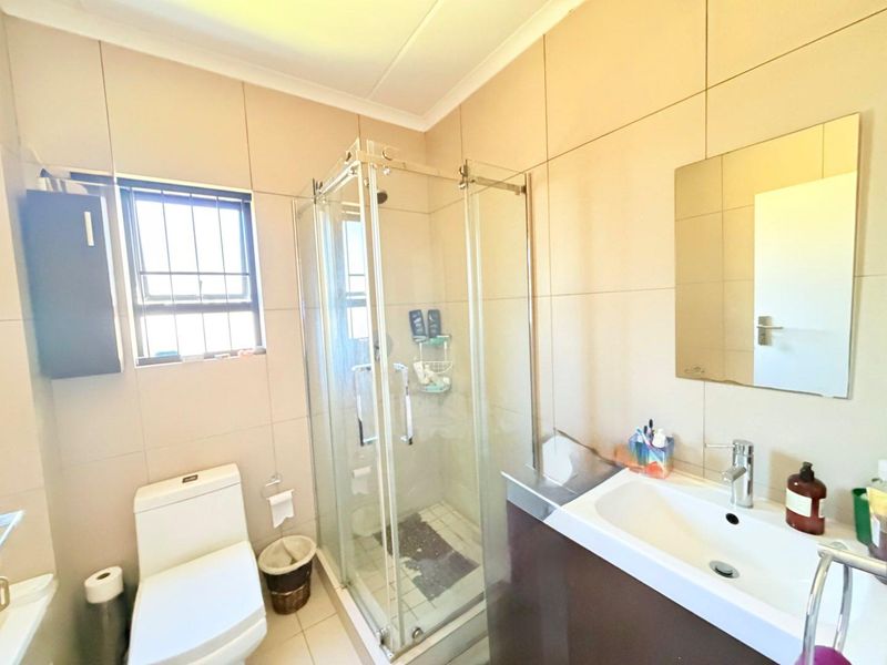 A functional bathroom featuring a glass shower enclosure, modern vanity with basin, wall-mounted mirror, and neutral wall tiling.