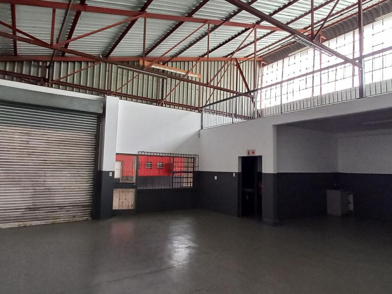 Spacious industrial utility area featuring high ceilings with exposed steel trusses, a large roller shutter door, and a functional mezzanine level.