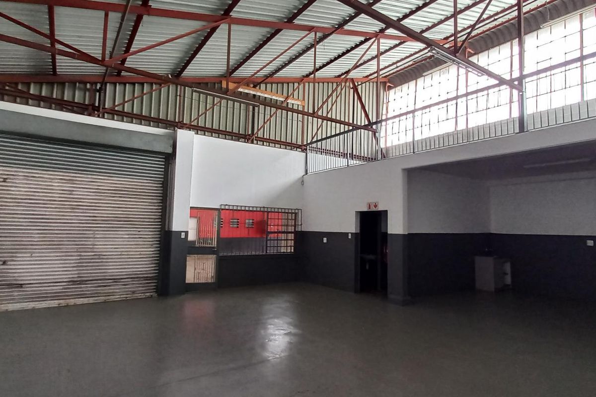 Spacious industrial utility area featuring high ceilings with exposed steel trusses, a large roller shutter door, and a functional mezzanine level.