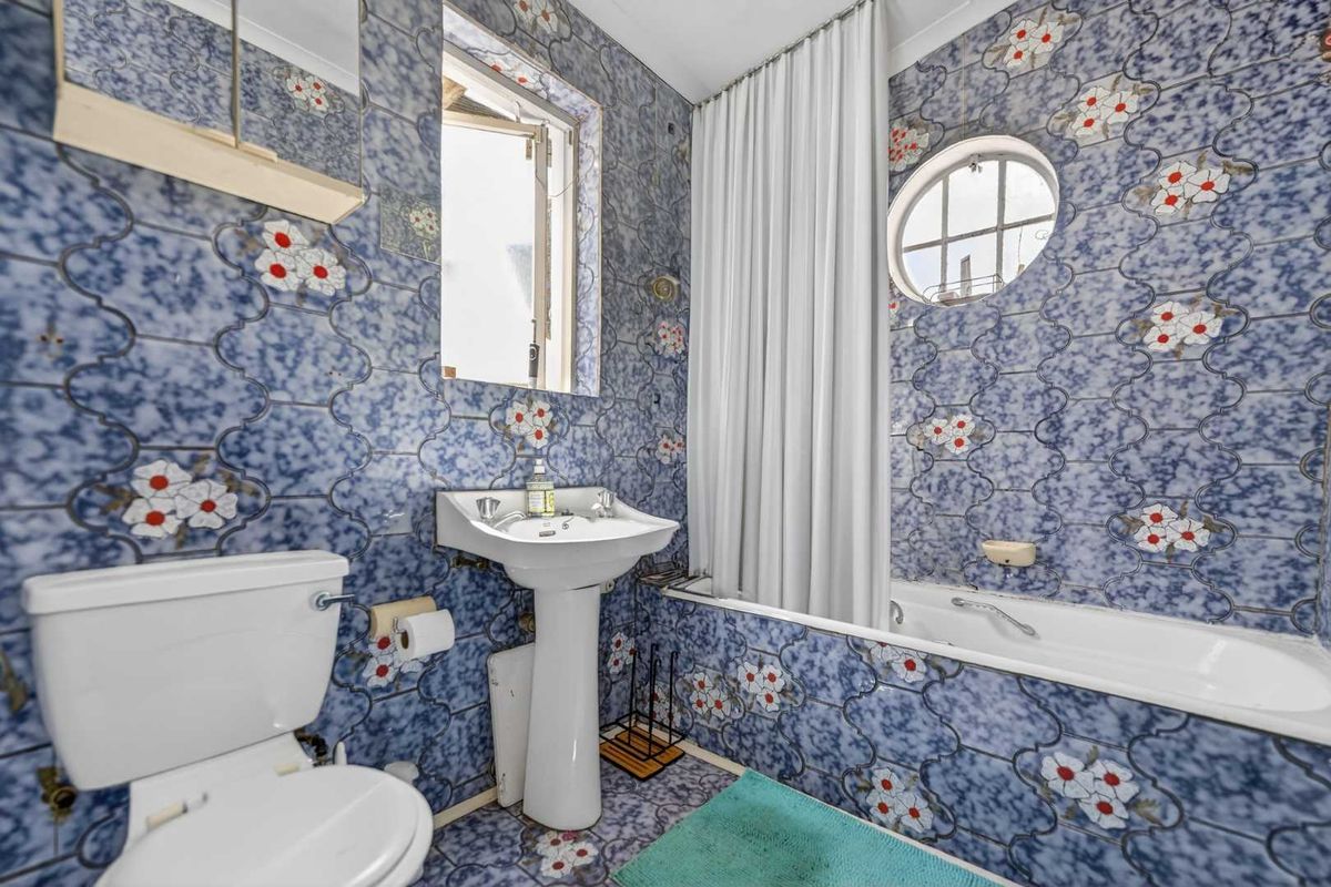 A dated bathroom featuring a pedestal sink, bathtub with shower curtain, and distinctive floral patterned wall and floor tiles.