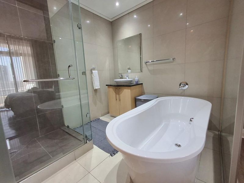 Modern bathroom featuring a freestanding bathtub, glass-enclosed shower, vessel sink with vanity cabinet, and neutral floor-to-ceiling tiling.