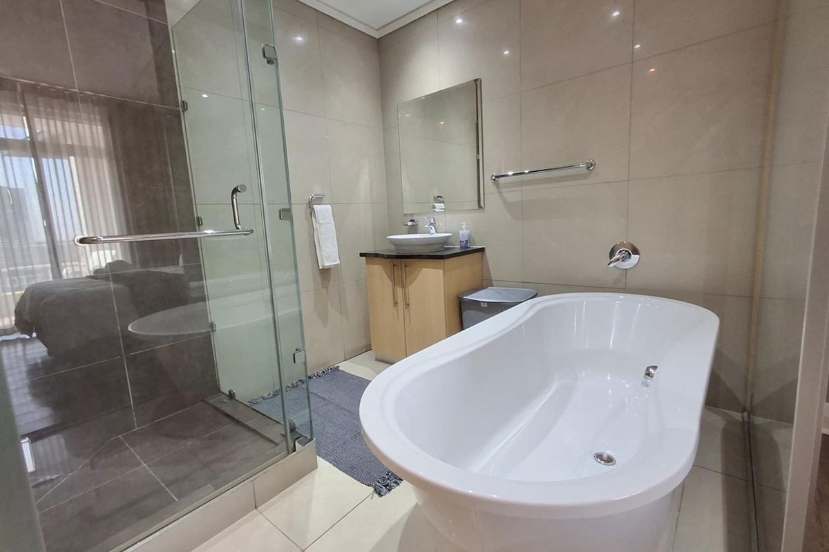 Modern bathroom featuring a freestanding bathtub, glass-enclosed shower, vessel sink with vanity cabinet, and neutral floor-to-ceiling tiling.