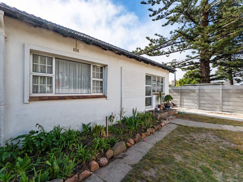 Rear exterior view of the house featuring a white plastered facade, tiled roof, and a concrete boundary wall with a garden pathway.