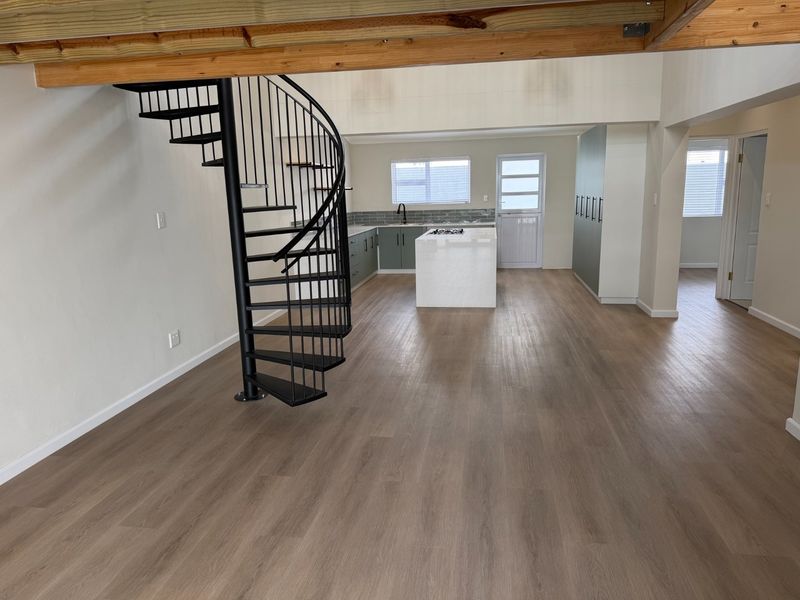 Spacious open-plan living area featuring a modern kitchen with island, sleek cabinetry, and a striking black spiral staircase leading to an upper level.
