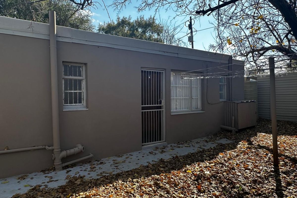 Rear exterior view of the property featuring a paved walkway, security gates on doors and windows, and a fixed outdoor washing line.
