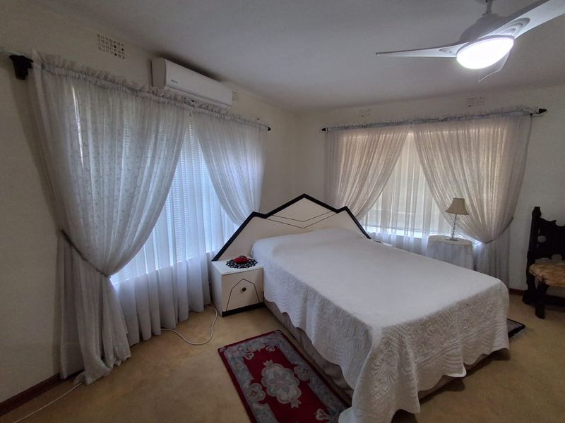 A well-lit bedroom featuring carpet flooring, a ceiling fan, and a wall-mounted split-system air conditioner.