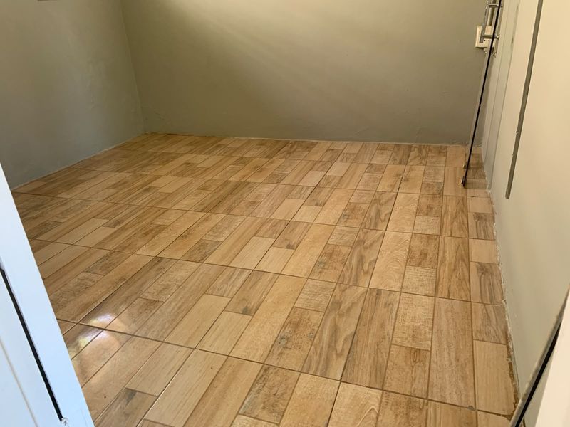 An empty room featuring wood-look ceramic floor tiles and plain painted walls, currently awaiting final finishes and baseboard installation.