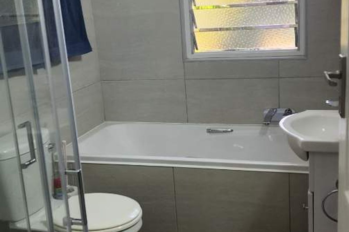 A functional bathroom featuring a bathtub, a separate glass-enclosed shower, a pedestal basin, and a louvered window for ventilation.