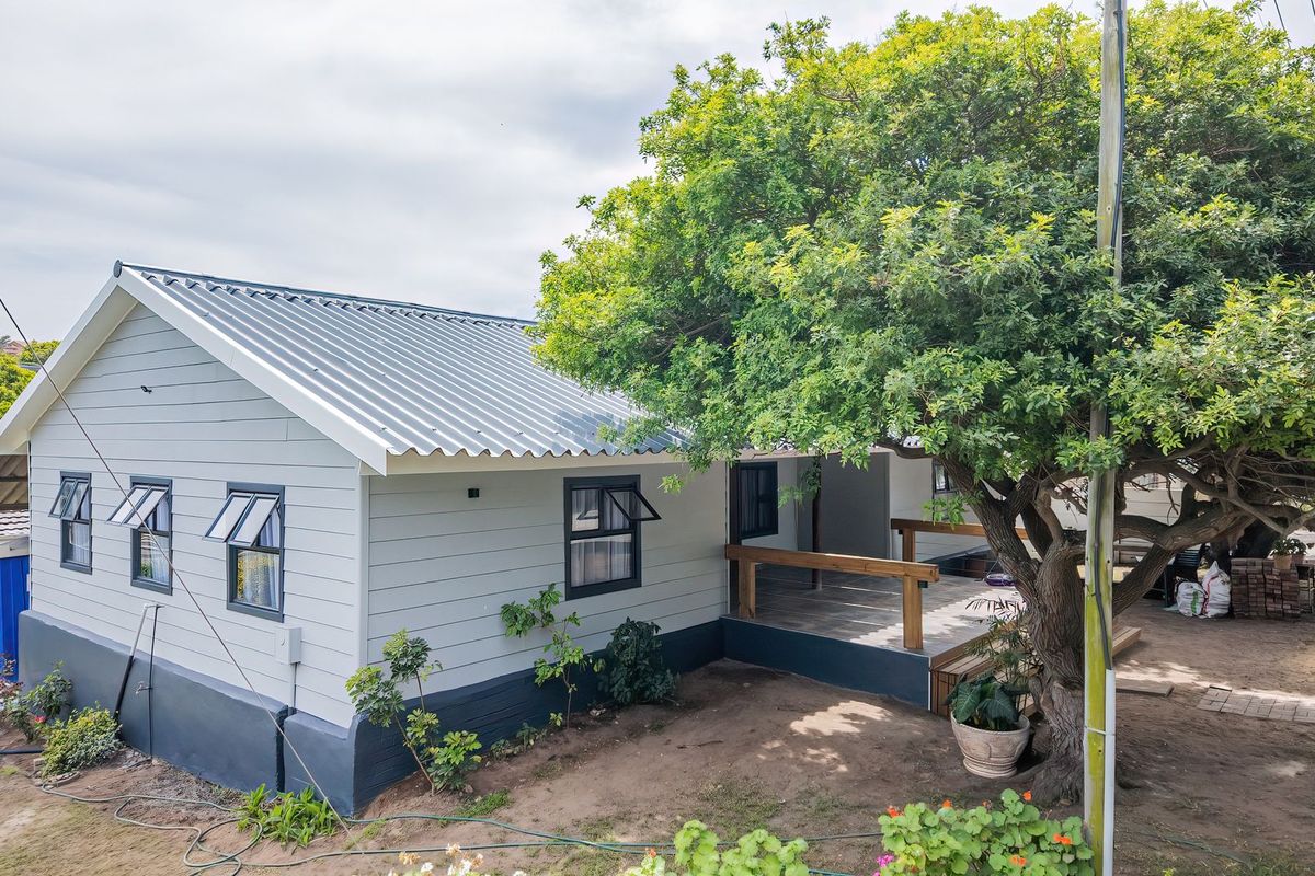 Rear view of the house featuring a timber deck, corrugated metal roof, and weatherboard cladding, set in a garden with a large mature tree.
