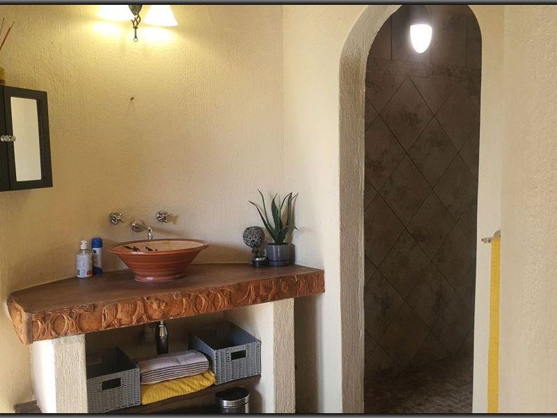 A rustic-style bathroom featuring a unique vessel sink on a custom stone vanity, leading through an arched doorway into a tiled shower area.
