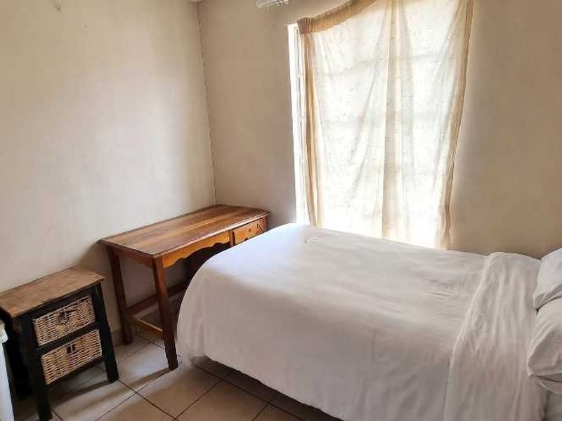 A compact bedroom featuring tiled flooring and a window with curtain rails, requiring minor cosmetic updates to the wall finishes.
