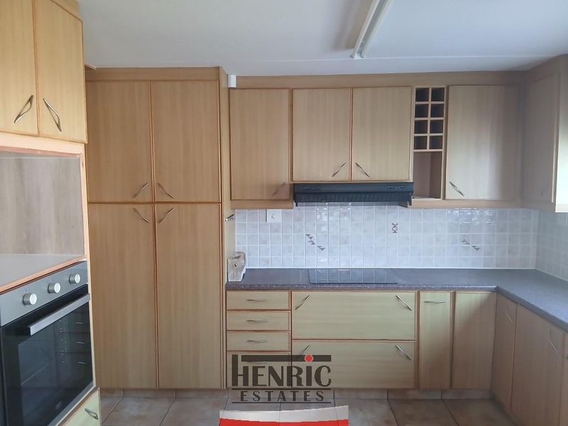 A functional kitchen featuring light wood-tone cabinetry, laminate countertops, a tiled backsplash, and integrated appliances including an oven, hob, and extractor fan.