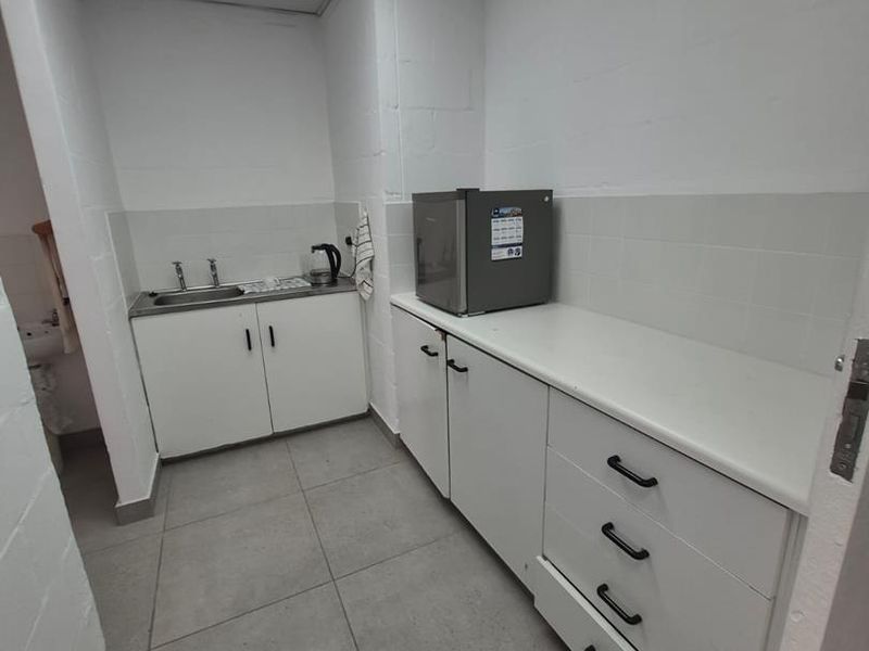 A functional office kitchenette featuring built-in white cabinetry, a stainless steel sink, tiled splashbacks, and durable floor tiles.