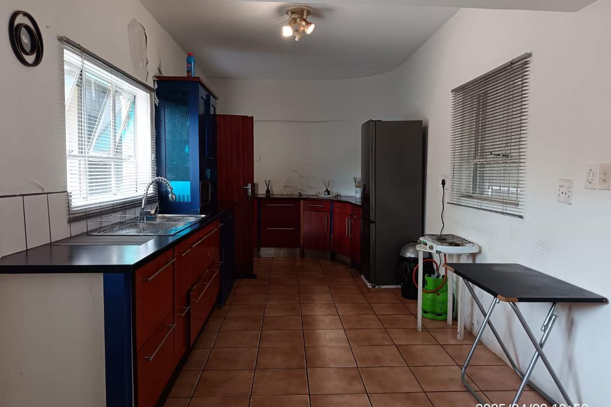 A functional kitchen featuring tiled flooring, built-in cabinetry, and a stainless steel sink, requiring cosmetic updates to improve its overall condition.