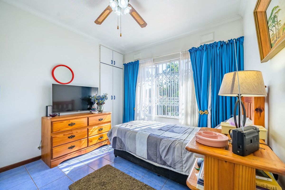 A bedroom featuring built-in cupboards, a ceiling fan, and tiled flooring, with a security gate installed on the window.