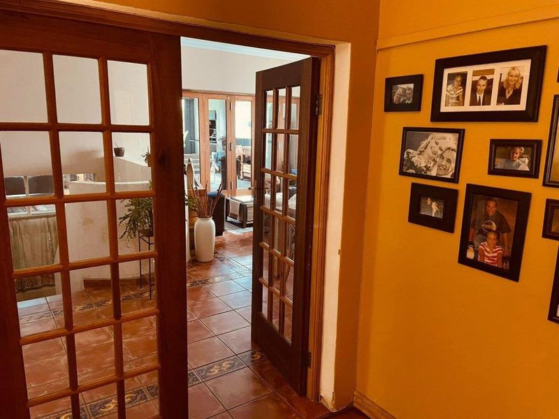 A hallway featuring terracotta floor tiles and wooden French doors leading into an adjacent living space.