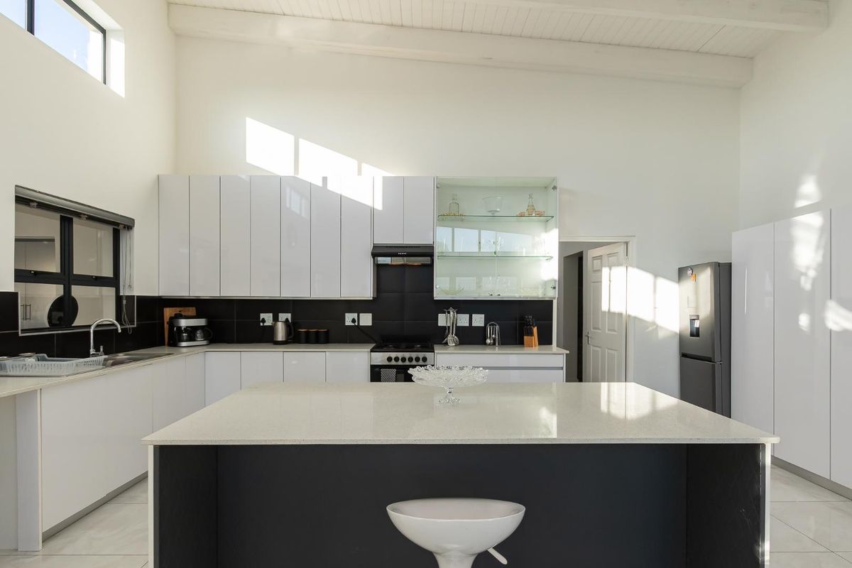 Modern kitchen featuring a central island with quartz countertops, high-gloss cabinetry, gas stove, and vaulted ceilings, offering a bright and contemporary culinary space.
