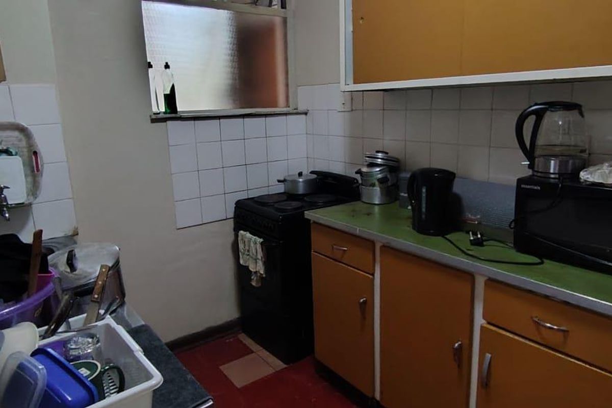 A compact, dated kitchen featuring original cabinetry, a tiled splashback, and a freestanding stove, offering potential for a modern renovation.
