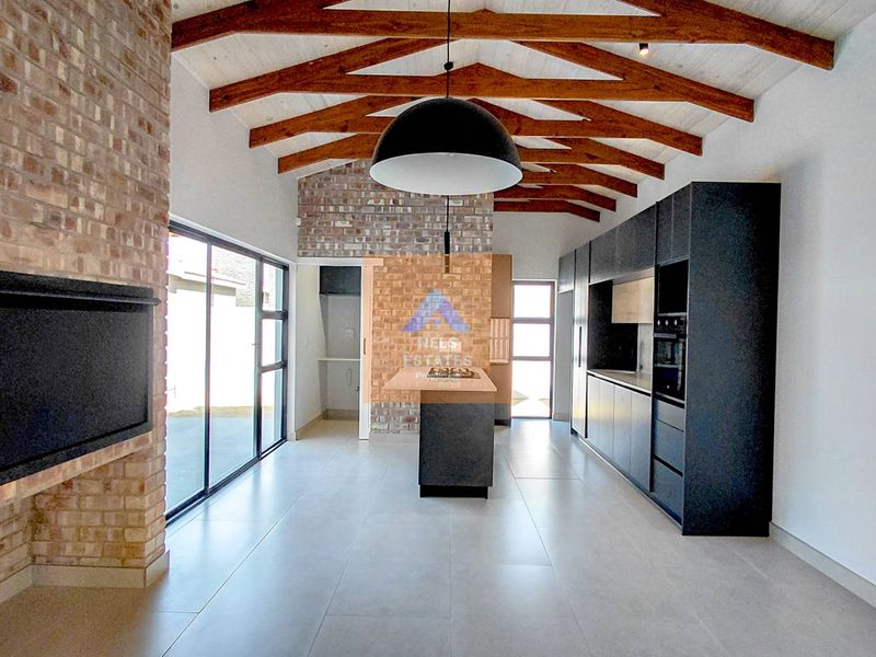 Spacious open-plan living and kitchen area featuring exposed timber trusses, a brick fireplace, modern cabinetry, and large sliding doors leading to the exterior.