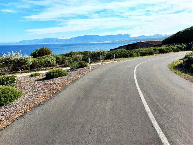 A scenic view of a paved coastal road winding through the landscape with ocean and mountain views in the background.