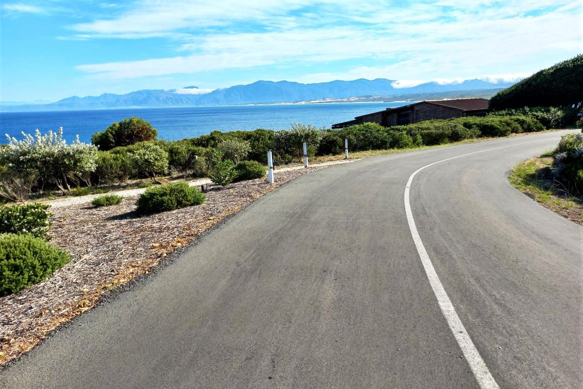 A scenic view of a paved coastal road winding through the landscape with ocean and mountain views in the background.