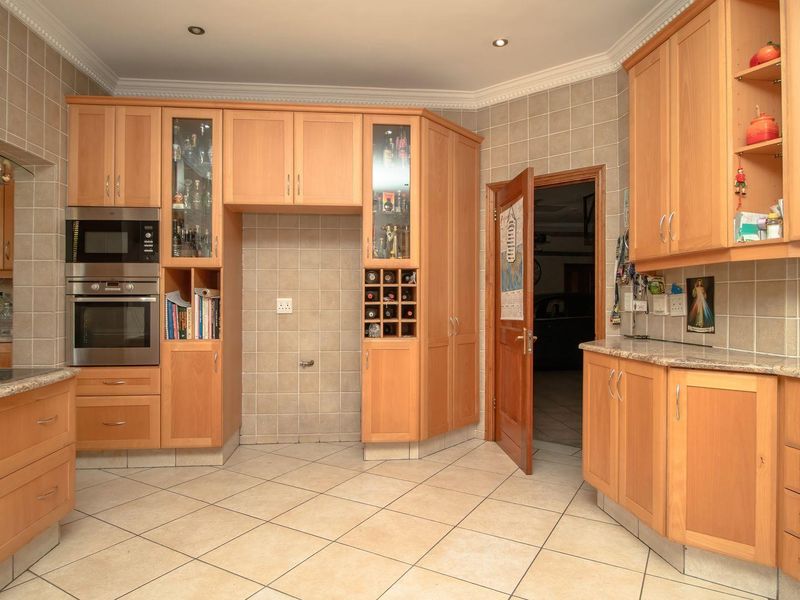 A functional kitchen featuring light wood cabinetry, granite countertops, built-in appliances, and tiled finishes throughout.