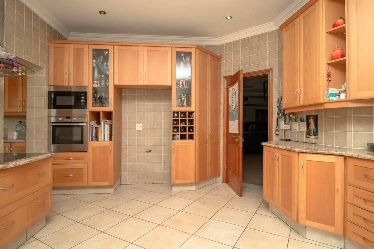 A functional kitchen featuring light wood cabinetry, granite countertops, built-in appliances, and tiled finishes throughout.