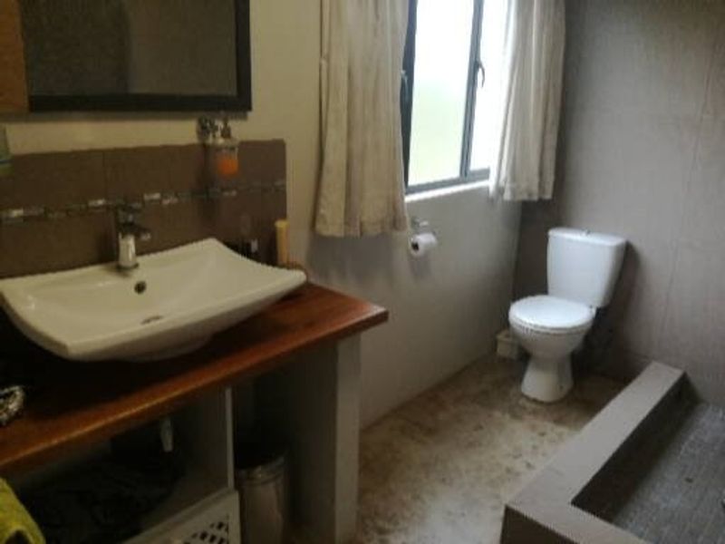 A functional bathroom featuring a vessel sink on a wooden vanity, a standard toilet, and a tiled shower base.