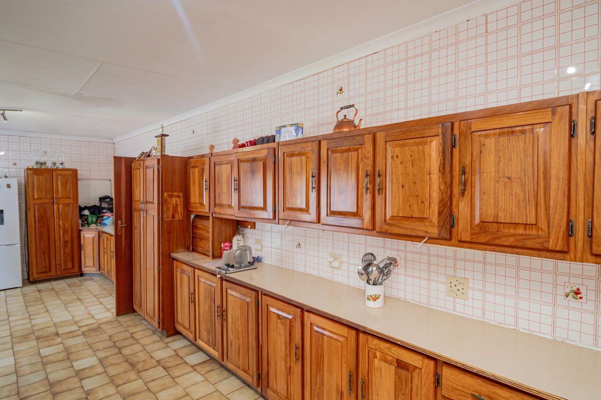 A spacious kitchen featuring extensive wooden cabinetry, tiled countertops, and ceramic wall tiles, offering a traditional farmhouse aesthetic with ample storage space.