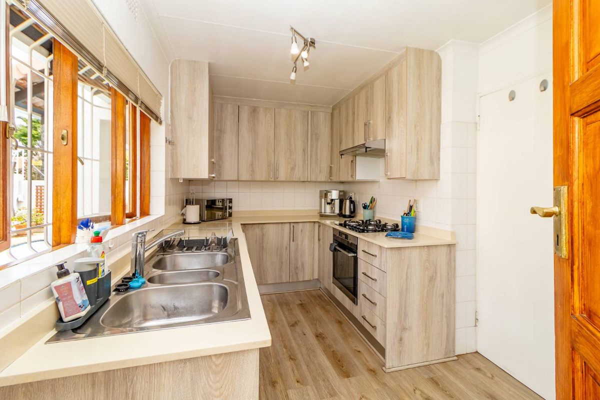 A functional kitchen featuring light wood-look cabinetry, a built-in oven with gas hob, extractor fan, and a double stainless steel sink.