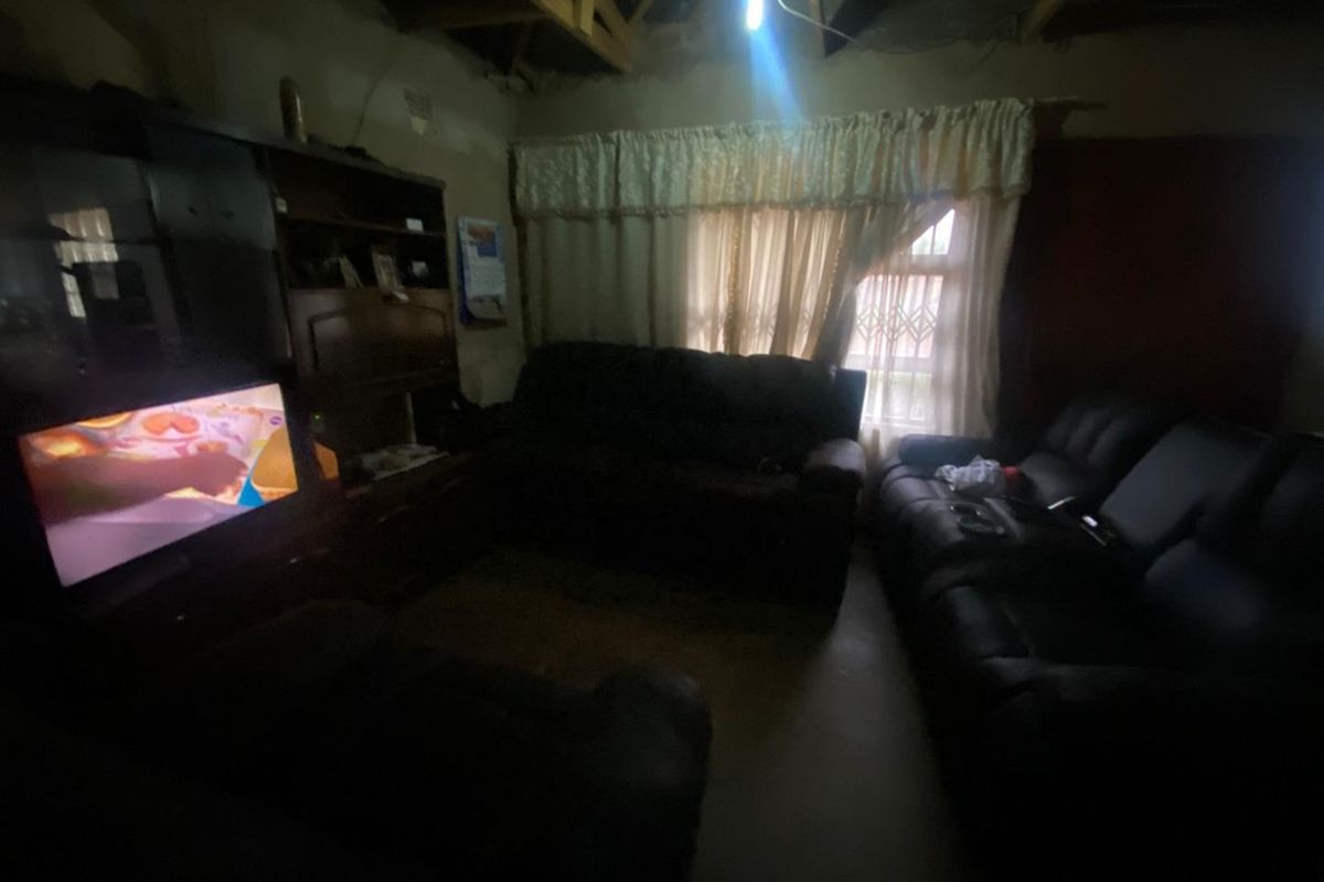 A living room space featuring exposed ceiling rafters and unfinished wall surfaces, requiring significant renovation and finishing work.