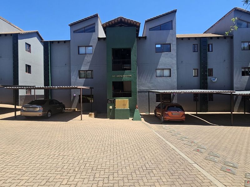 Front elevation of a multi-story apartment complex featuring paved parking areas and covered carports.
