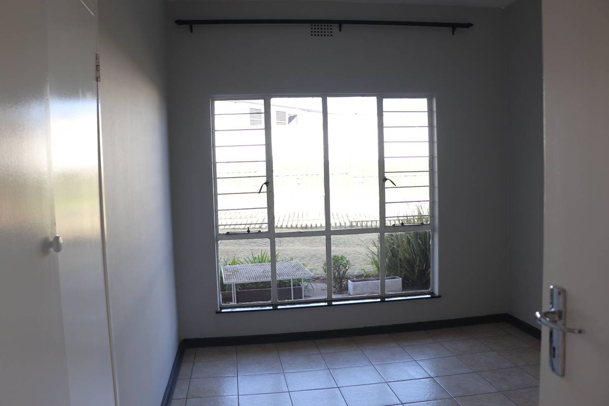 An empty bedroom featuring tiled flooring, security bars on the window, and a built-in cupboard, offering a clean and neutral space.