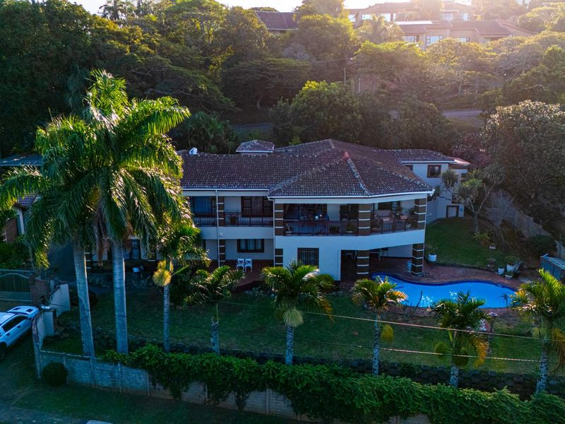 Aerial view of a multi-story residential property featuring a tiled roof, spacious balconies, a swimming pool, and established garden landscaping.