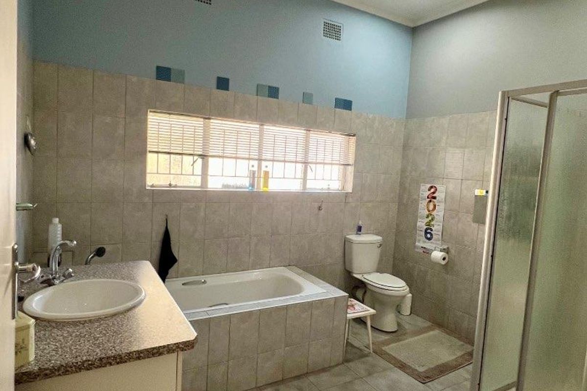 A functional bathroom featuring a built-in bathtub, separate glass-enclosed shower, vanity basin, and toilet with neutral wall and floor tiling.