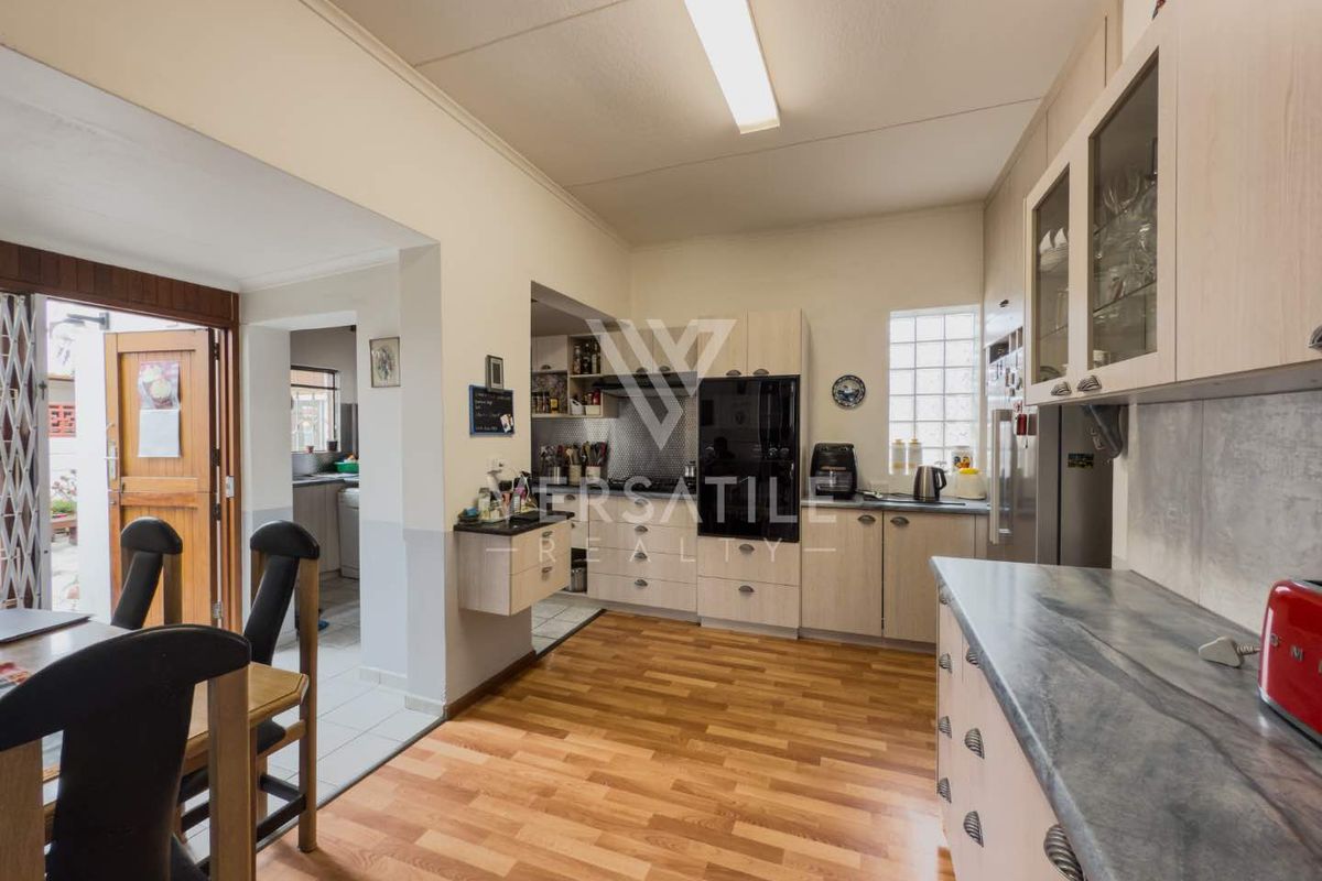 A functional kitchen featuring light wood cabinetry, laminate countertops, and a built-in oven, with an adjacent dining area and access to a scullery.