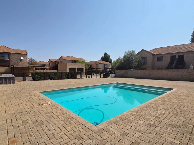 Communal swimming pool area featuring paved surround and perimeter walling within a townhouse complex.