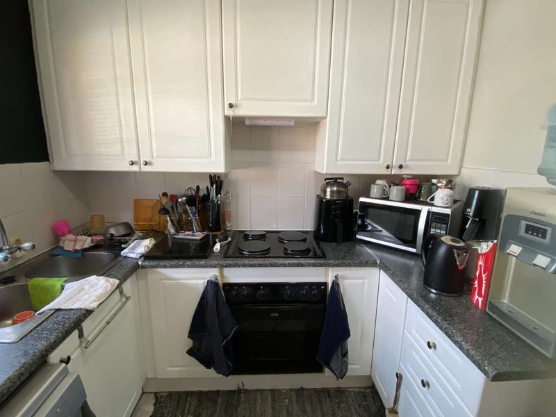 A functional kitchen featuring white cabinetry, dark laminate countertops, a built-in oven, electric hob, and a stainless steel sink with tiled splashback.