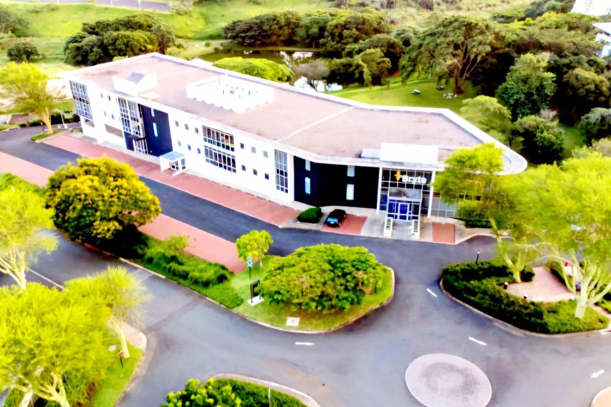 Aerial view of a modern office building complex featuring landscaped grounds, paved driveway, and ample parking space in a serene setting.