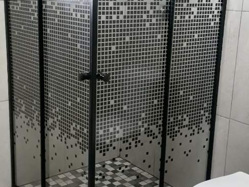 Modern bathroom featuring a corner shower enclosure with a black frame, rain shower head, and a white toilet with tiled finishes.